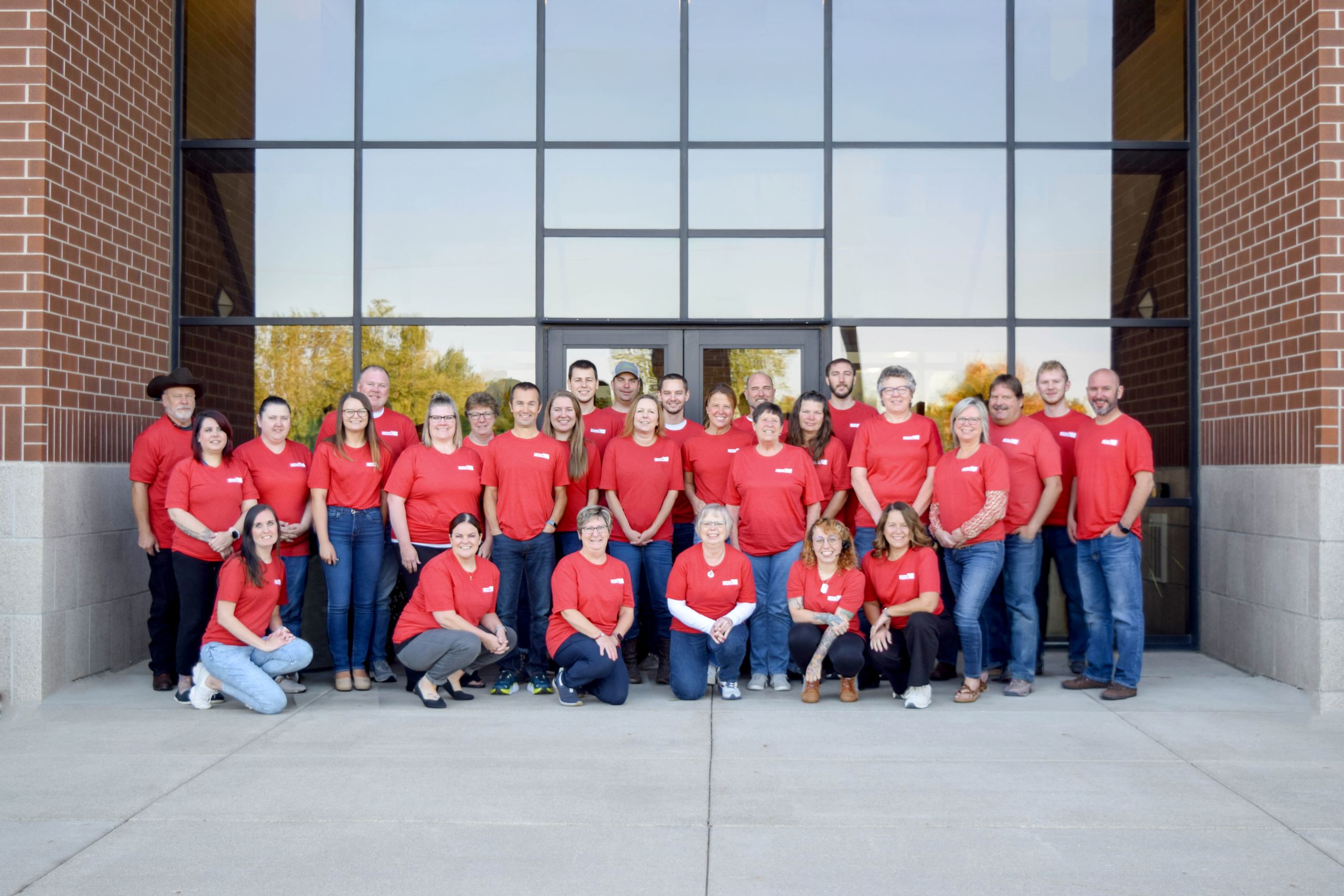 Western Products Team Photo Group of Western Products employees wearing red shirts and posing in front of the company's office building entrance.